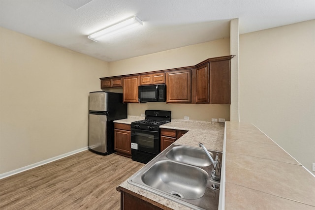 kitchen with a sink, baseboards, light countertops, light wood-type flooring, and black appliances