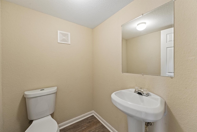 bathroom featuring baseboards, a textured ceiling, toilet, and wood finished floors