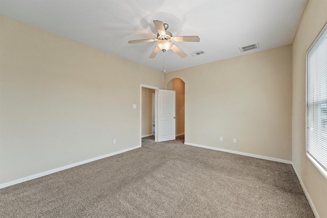 unfurnished room with arched walkways, carpet floors, a ceiling fan, visible vents, and baseboards