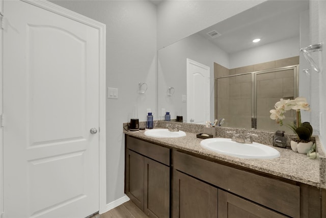 bathroom with double vanity, wood finished floors, a stall shower, and a sink