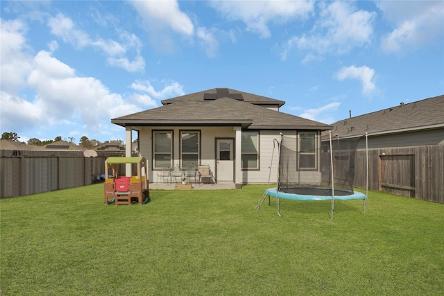 rear view of house with a fenced backyard, a trampoline, and a lawn