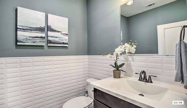 half bath featuring toilet, vanity, visible vents, and tile walls