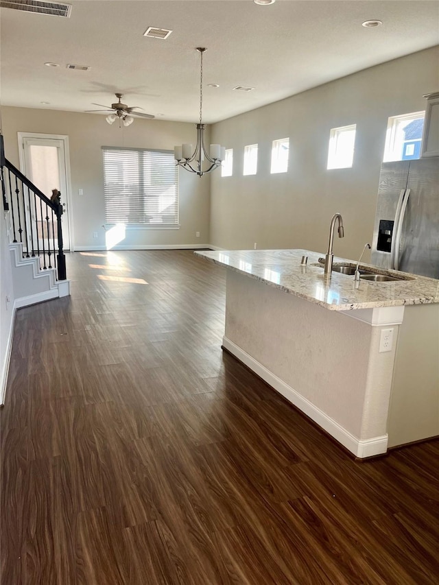 kitchen with light stone counters, a center island with sink, baseboards, dark wood finished floors, and a sink