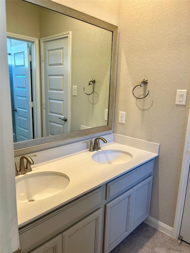 bathroom with double vanity, a textured wall, baseboards, and a sink