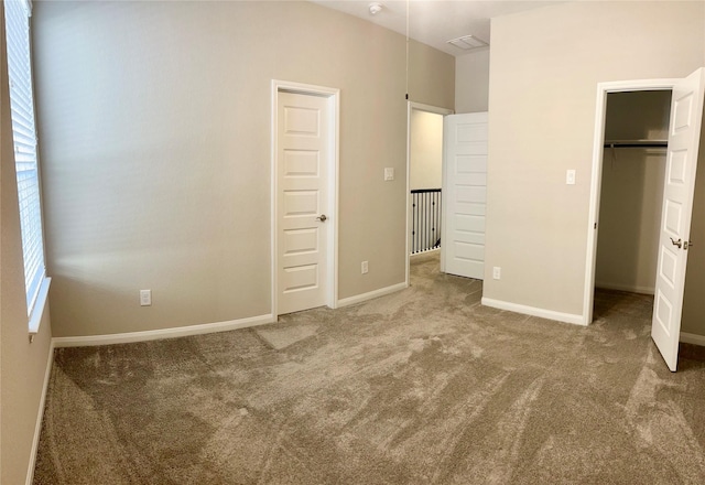 unfurnished bedroom featuring a closet, carpet flooring, a walk in closet, and baseboards