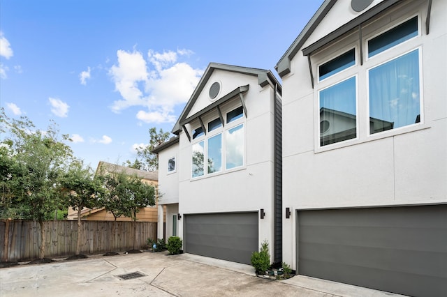 view of home's exterior with stucco siding, driveway, a garage, and fence