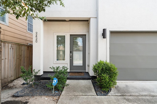 property entrance featuring a garage, stucco siding, and fence