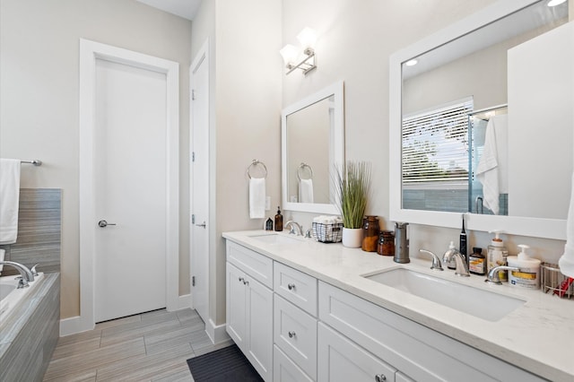 bathroom with double vanity, a relaxing tiled tub, baseboards, and a sink