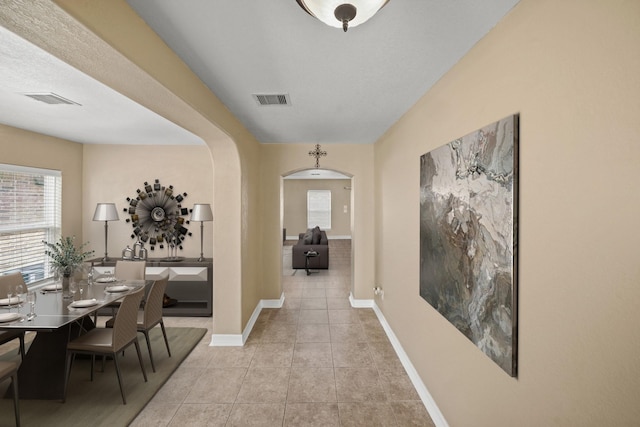 corridor with light tile patterned floors, visible vents, arched walkways, and baseboards