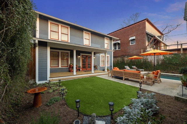 back of house at dusk with an outdoor hangout area, a patio, french doors, and a lawn