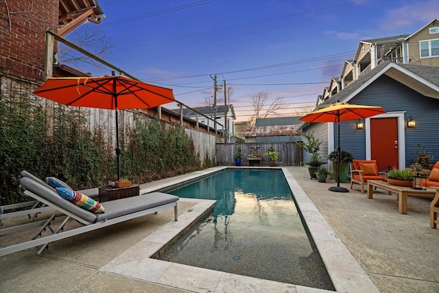 pool at dusk with a patio area, a fenced backyard, and a fenced in pool