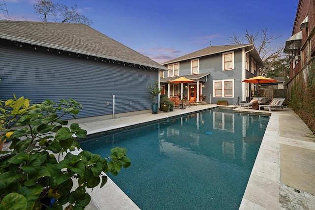 pool at dusk with an outdoor pool, a patio area, and fence