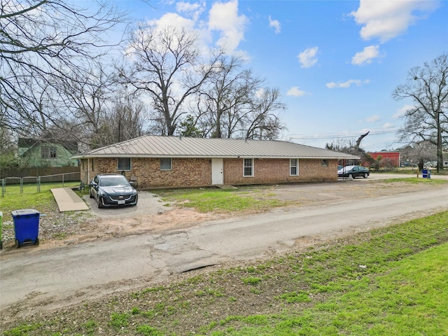 view of front of property featuring dirt driveway, metal roof, fence, a front lawn, and brick siding