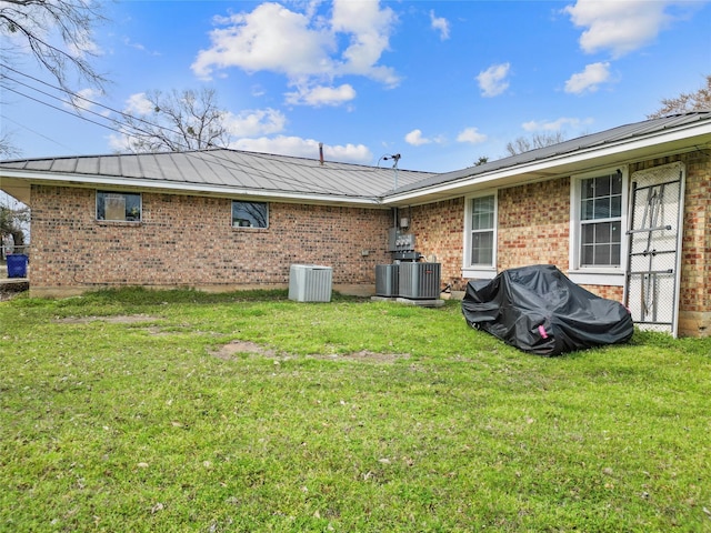 back of house featuring brick siding, metal roof, central AC, and a yard