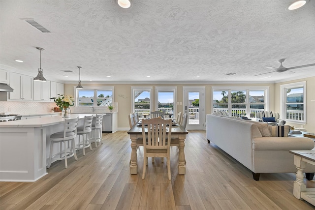 dining space with light wood-type flooring, a textured ceiling, visible vents, and crown molding