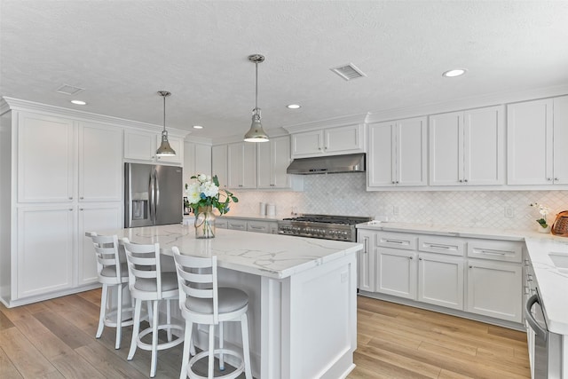 kitchen featuring stainless steel appliances, visible vents, white cabinets, a kitchen island, and under cabinet range hood