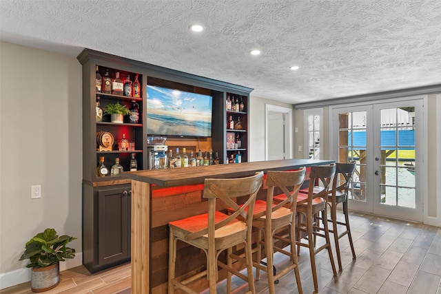 bar featuring a dry bar, wood tiled floor, a textured ceiling, french doors, and recessed lighting