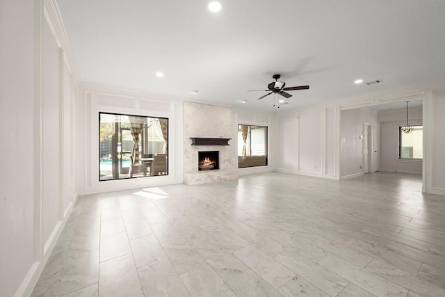 unfurnished living room with a decorative wall, a healthy amount of sunlight, a brick fireplace, and ceiling fan