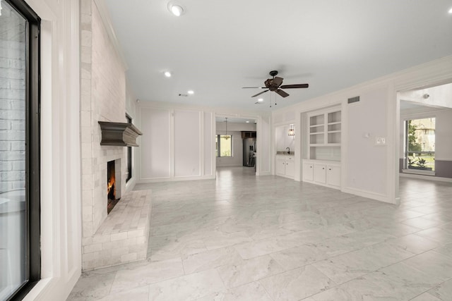 unfurnished living room with visible vents, built in shelves, a large fireplace, ceiling fan, and marble finish floor