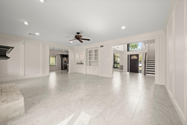 unfurnished living room with stairway, built in shelves, a ceiling fan, a decorative wall, and marble finish floor