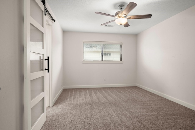 empty room featuring visible vents, baseboards, carpet, a barn door, and a ceiling fan