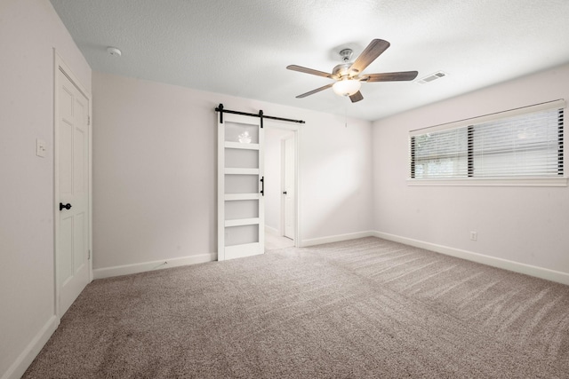 unfurnished bedroom featuring visible vents, a textured ceiling, a barn door, carpet flooring, and baseboards