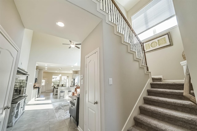 staircase featuring baseboards, a ceiling fan, tile patterned floors, a high ceiling, and recessed lighting