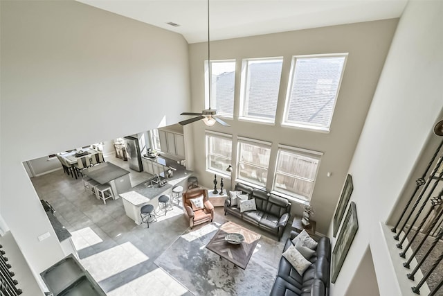 living room featuring ceiling fan, visible vents, stairs, and a towering ceiling