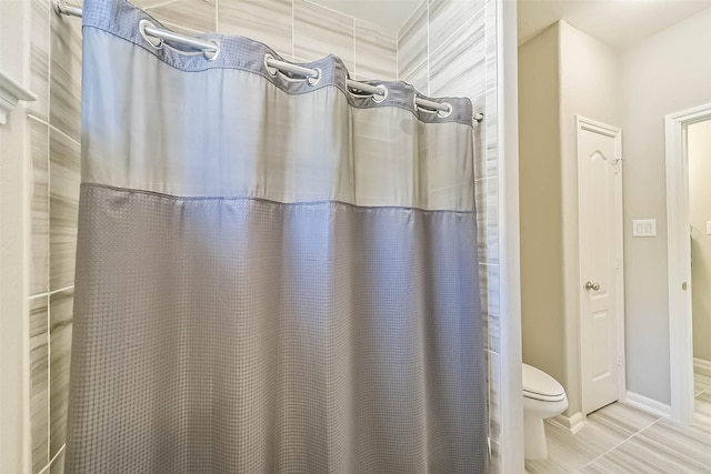 bathroom featuring curtained shower, baseboards, and toilet