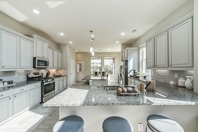 kitchen with appliances with stainless steel finishes, a peninsula, a kitchen bar, and light stone countertops