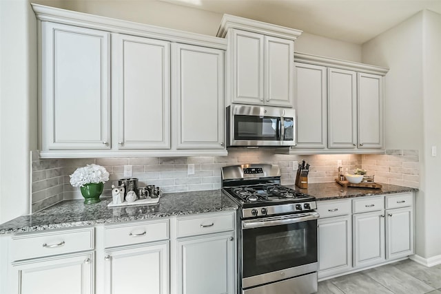 kitchen with light tile patterned floors, white cabinetry, appliances with stainless steel finishes, backsplash, and dark stone counters