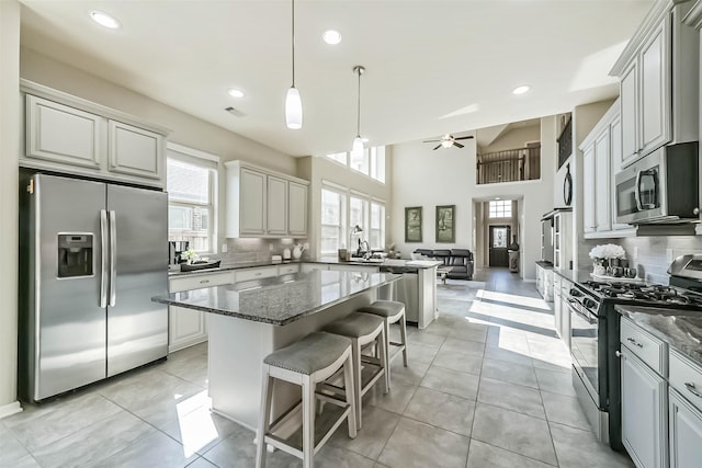 kitchen featuring light tile patterned floors, stainless steel appliances, a kitchen island, decorative backsplash, and dark stone countertops