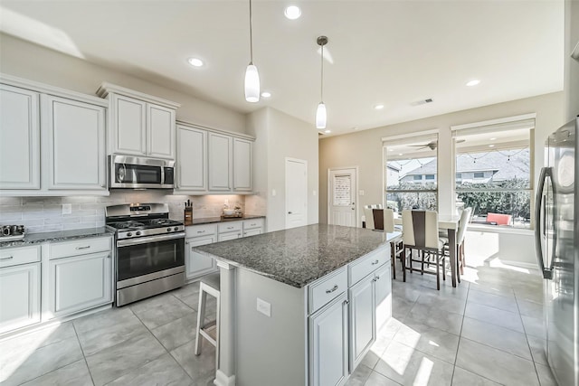 kitchen featuring light tile patterned floors, a kitchen island, appliances with stainless steel finishes, backsplash, and dark stone countertops