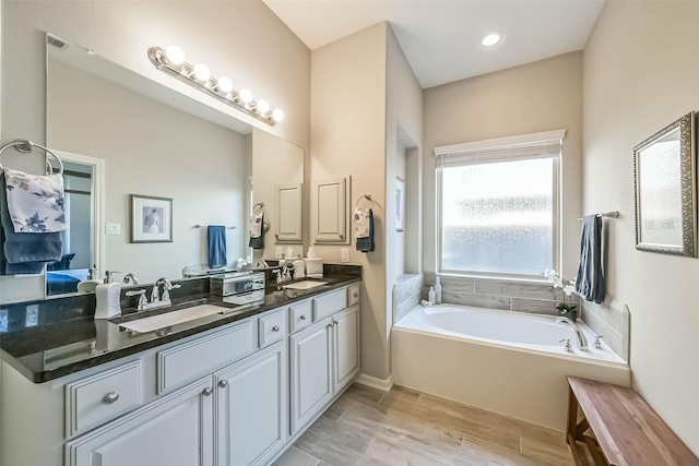 full bathroom featuring a garden tub, double vanity, wood finished floors, and a sink