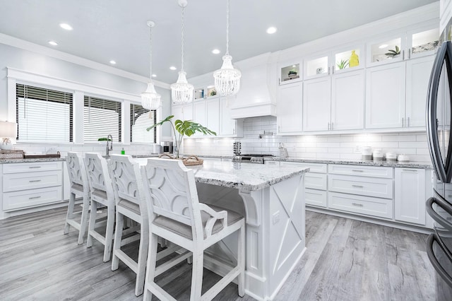 636 Villa Dr, Crystal Beach, TX 77650 - kitchen with tasteful backsplash, white cabinets, an island with sink, custom range hood, and ornamental molding
