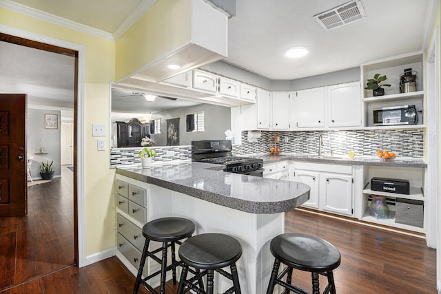 kitchen with black range with gas cooktop, visible vents, a breakfast bar area, a peninsula, and a sink