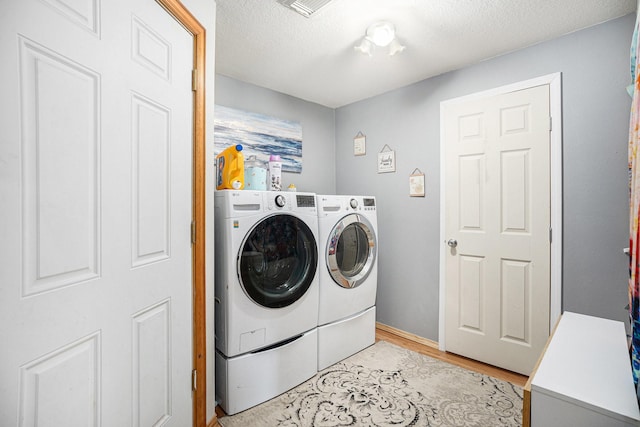 washroom featuring a textured ceiling, laundry area, washing machine and dryer, and light wood-style flooring