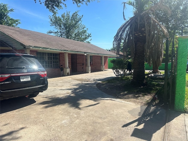 view of side of property with driveway, brick siding, and a shingled roof