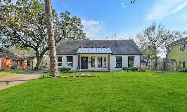 view of front facade with central AC unit, a standing seam roof, metal roof, fence, and a front lawn