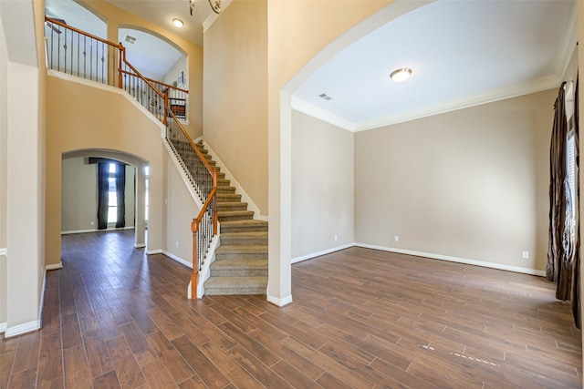 entrance foyer with dark wood-style floors, arched walkways, stairway, ornamental molding, and baseboards