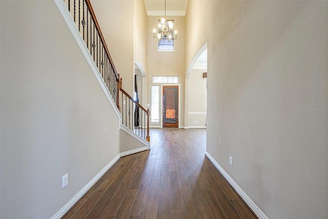 foyer featuring a notable chandelier, dark wood-style flooring, a towering ceiling, baseboards, and stairs