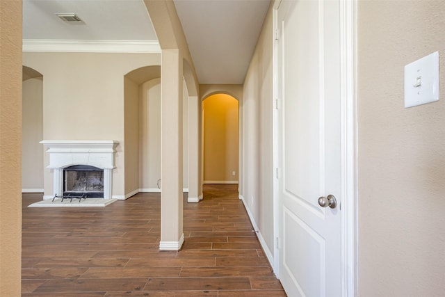 corridor featuring arched walkways, wood finished floors, visible vents, baseboards, and crown molding