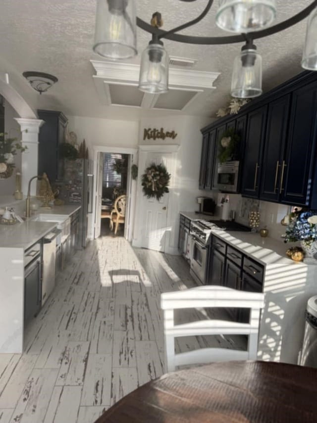 kitchen with light countertops, appliances with stainless steel finishes, dark cabinetry, a textured ceiling, and a sink