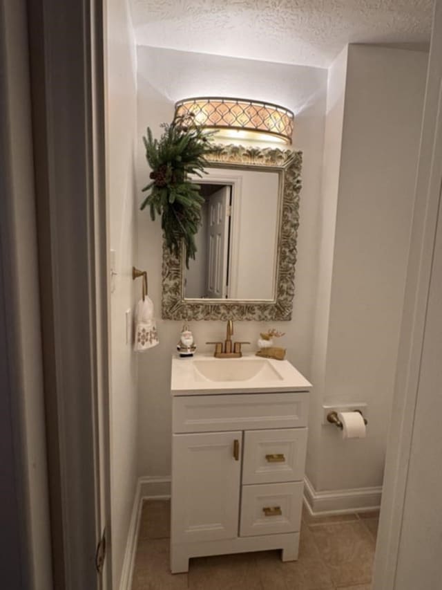 half bathroom featuring a textured ceiling, tile patterned flooring, vanity, and baseboards