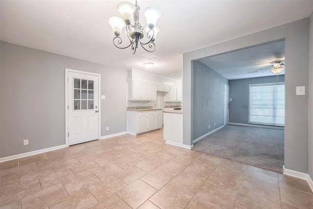 interior space with light tile patterned flooring, ceiling fan with notable chandelier, white cabinetry, baseboards, and open floor plan