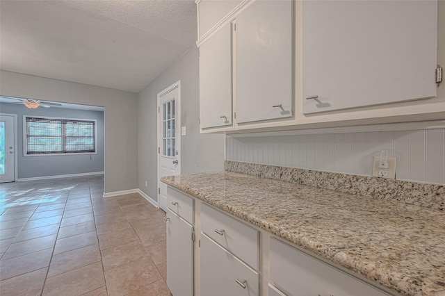 kitchen with light tile patterned floors, ceiling fan, a textured ceiling, baseboards, and white cabinets