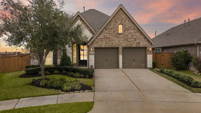 french provincial home with driveway, stone siding, fence, and brick siding