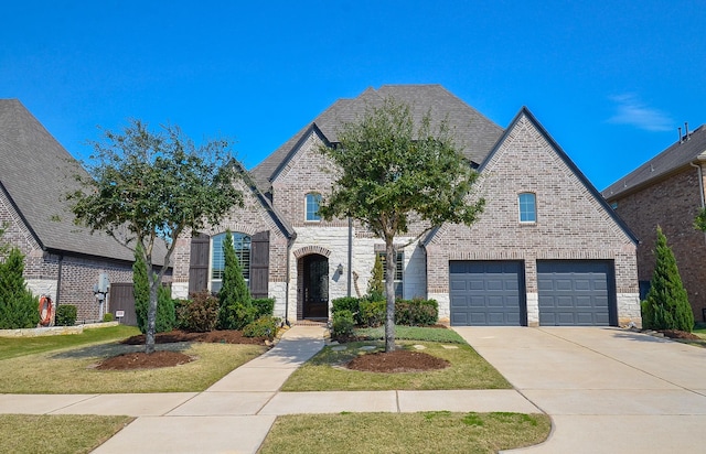 french country inspired facade featuring driveway, brick siding, stone siding, and a shingled roof