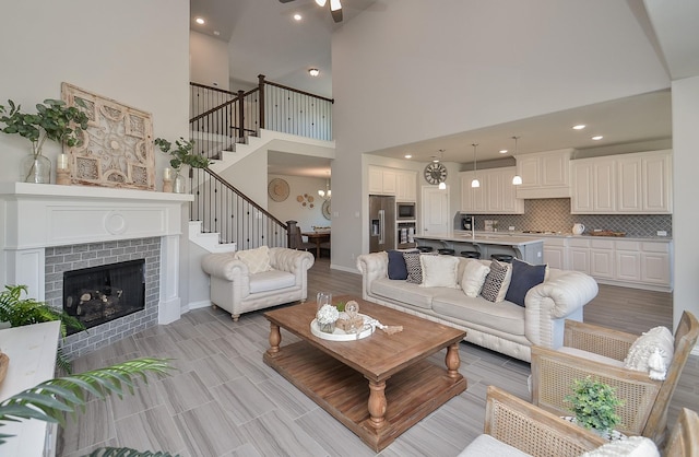 living area with recessed lighting, a tiled fireplace, light wood-style floors, baseboards, and stairs