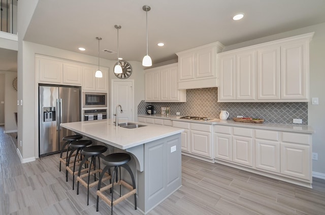 kitchen featuring light countertops, decorative backsplash, appliances with stainless steel finishes, white cabinetry, and a sink